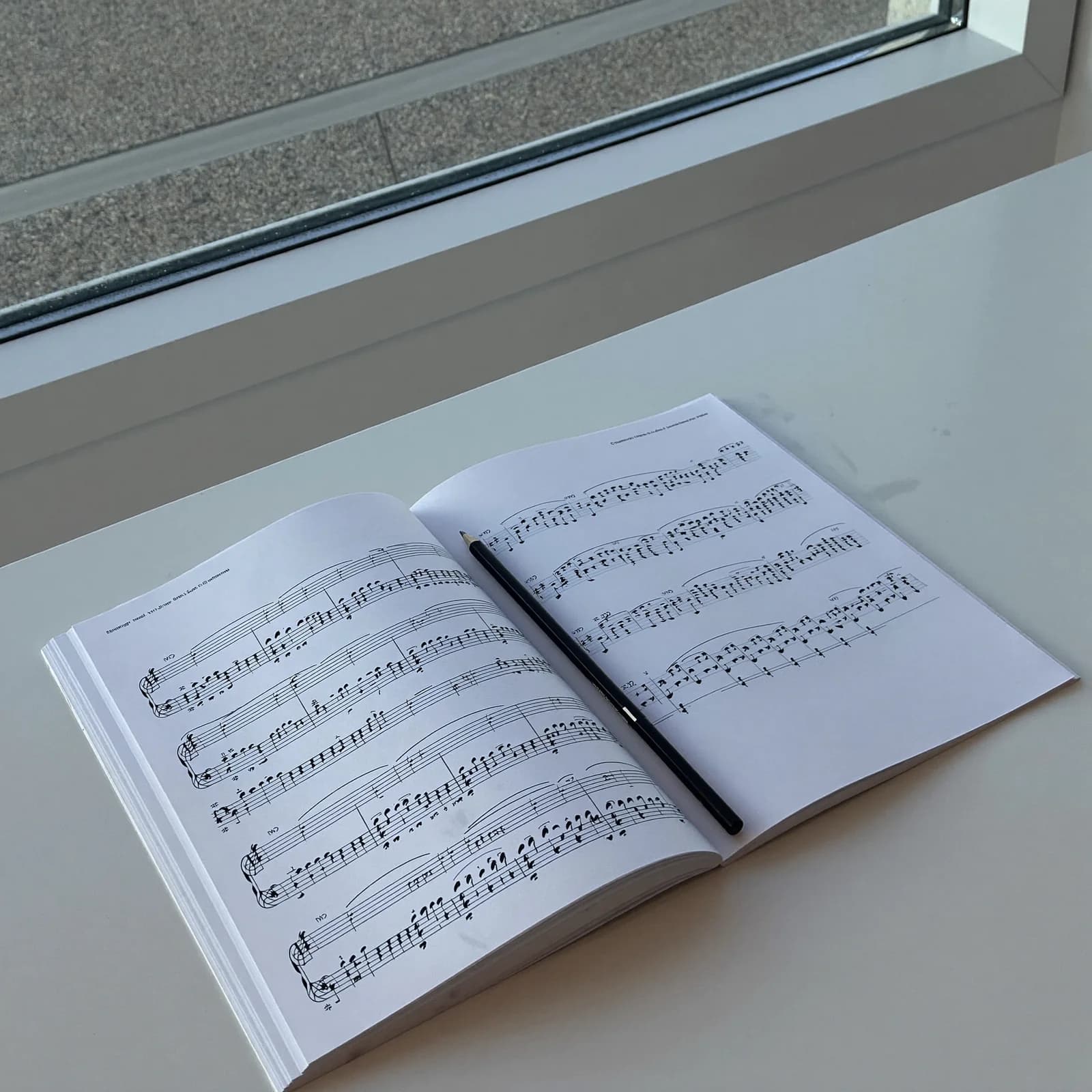 An open choral score on a white table in soft daylight, a pencil resting on the page